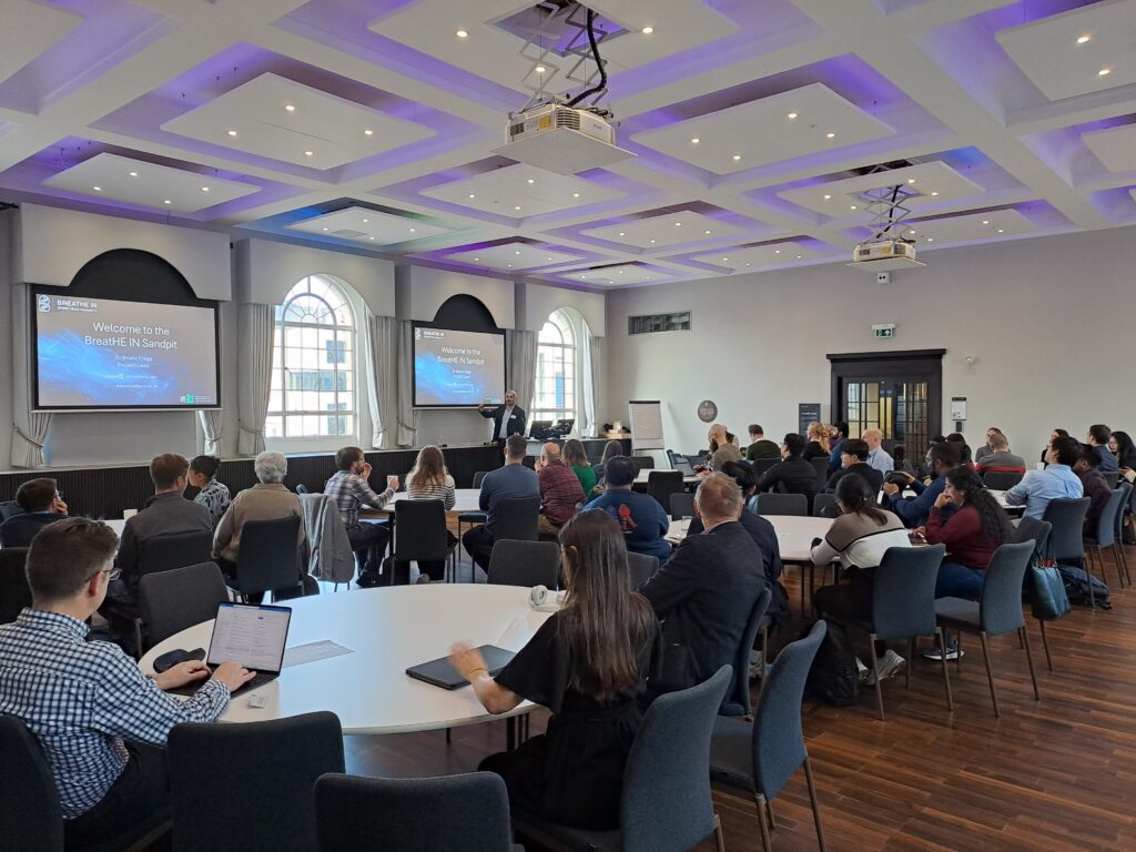 Scene of individuals attending sandpit day at tables watching presentation
